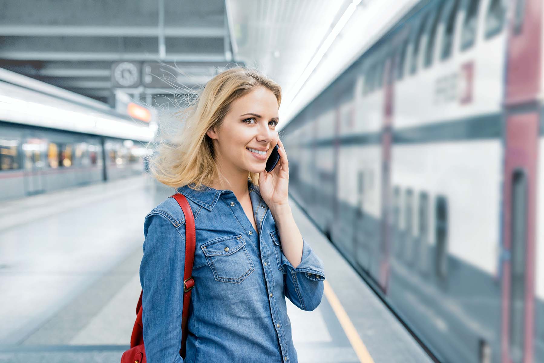 Frau telefoniert mit ihrem Handy am Bahnsteig