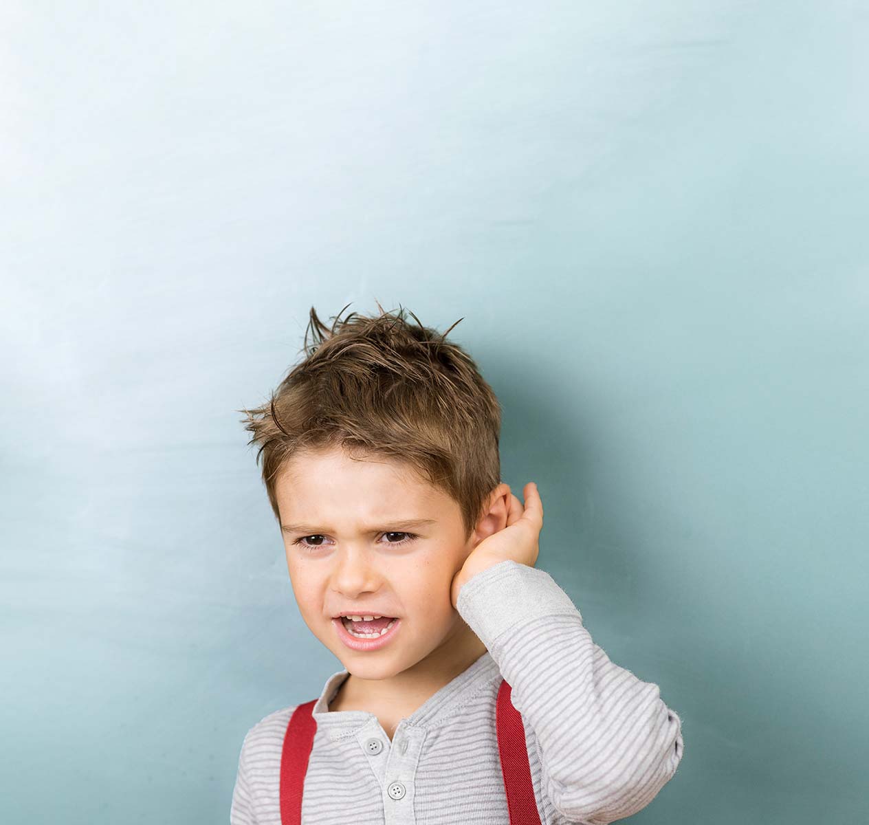 Ein Junge mit Hosenträgern hält sich die Hand ans Ohr.