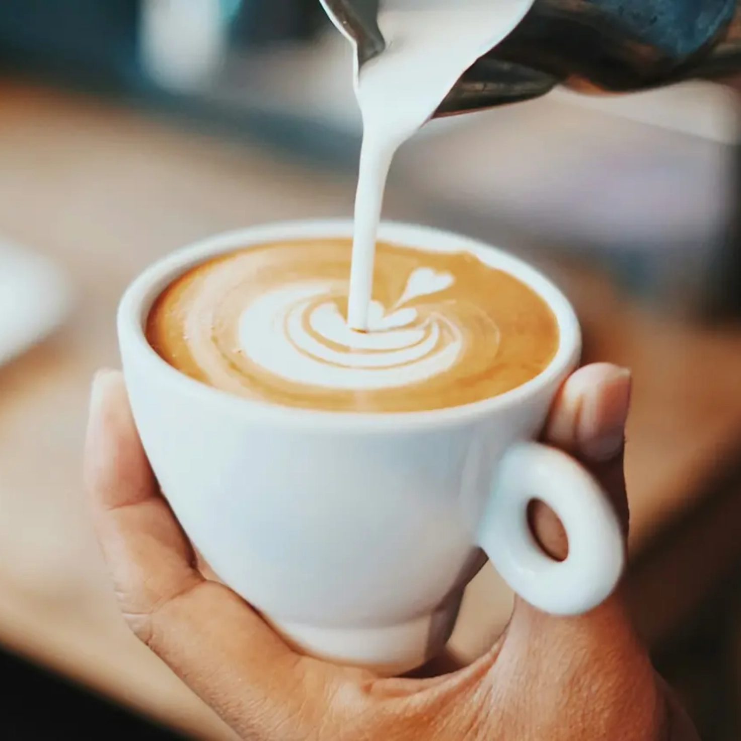 Tasse mit Kaffee, in die Milch eingegossen wird