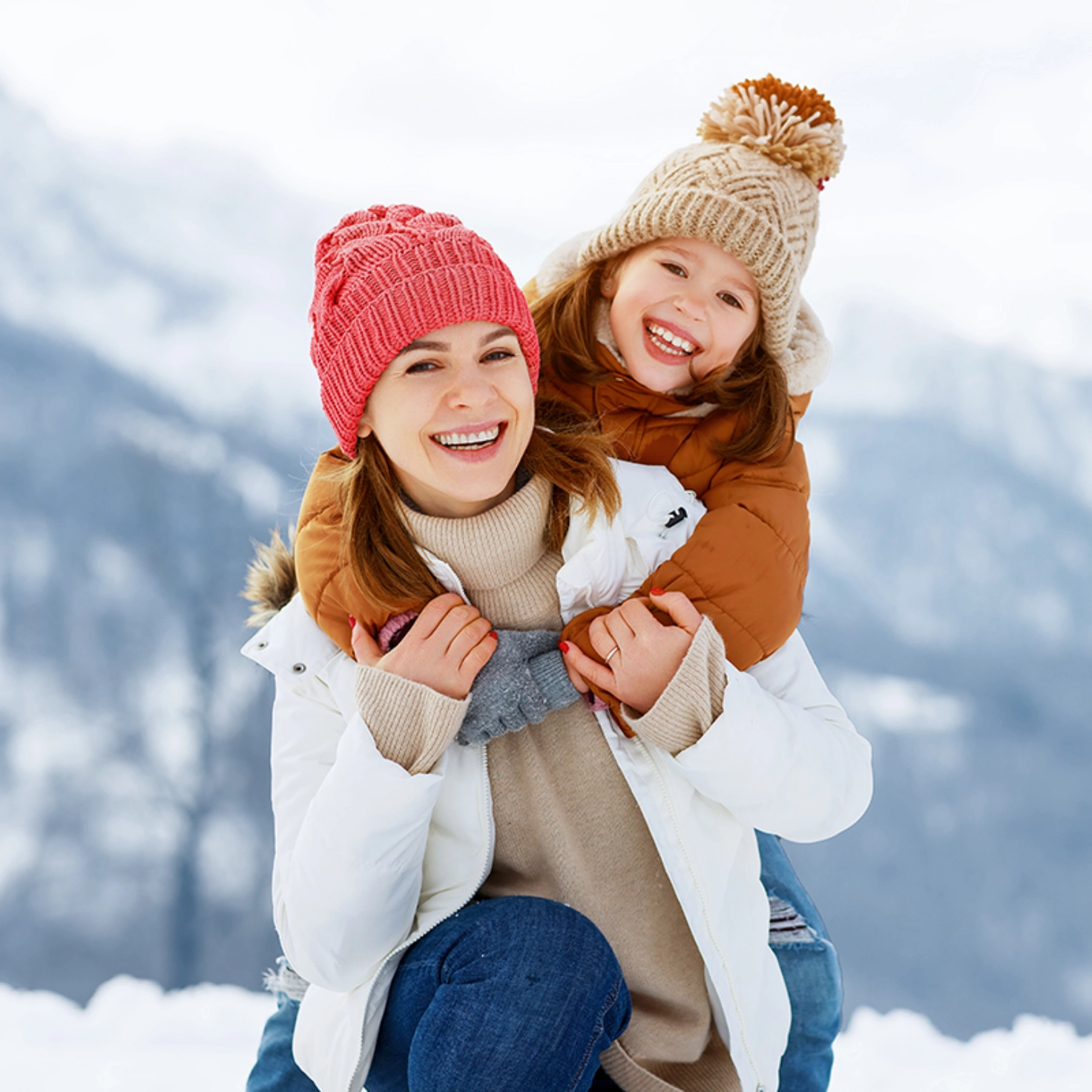Mutter kniet im Schnee und Tochter umarmt sie von hinten