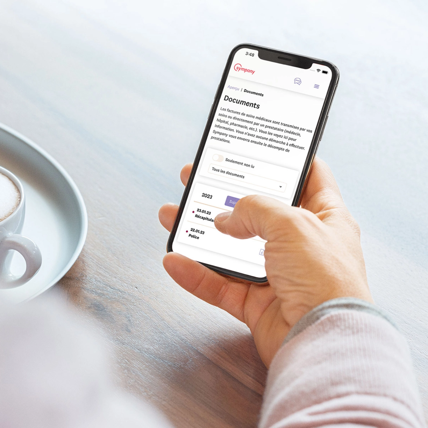 Une personne tient un smartphone dans sa main. On peut voir à l'écran le portail clients mySympany en version française.