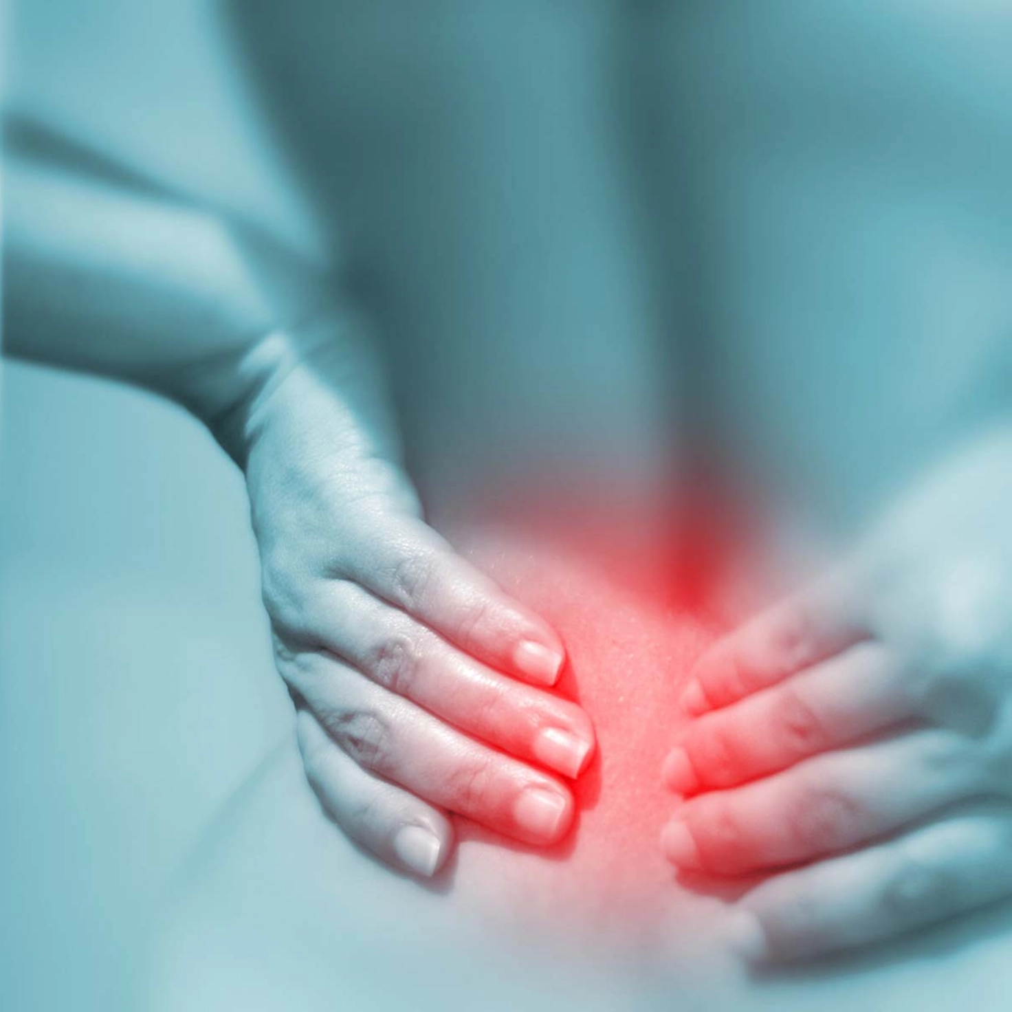 A person from behind in shades of grey. The person is holding their lower back with both hands. The lower back is marked in red to visualise pain.