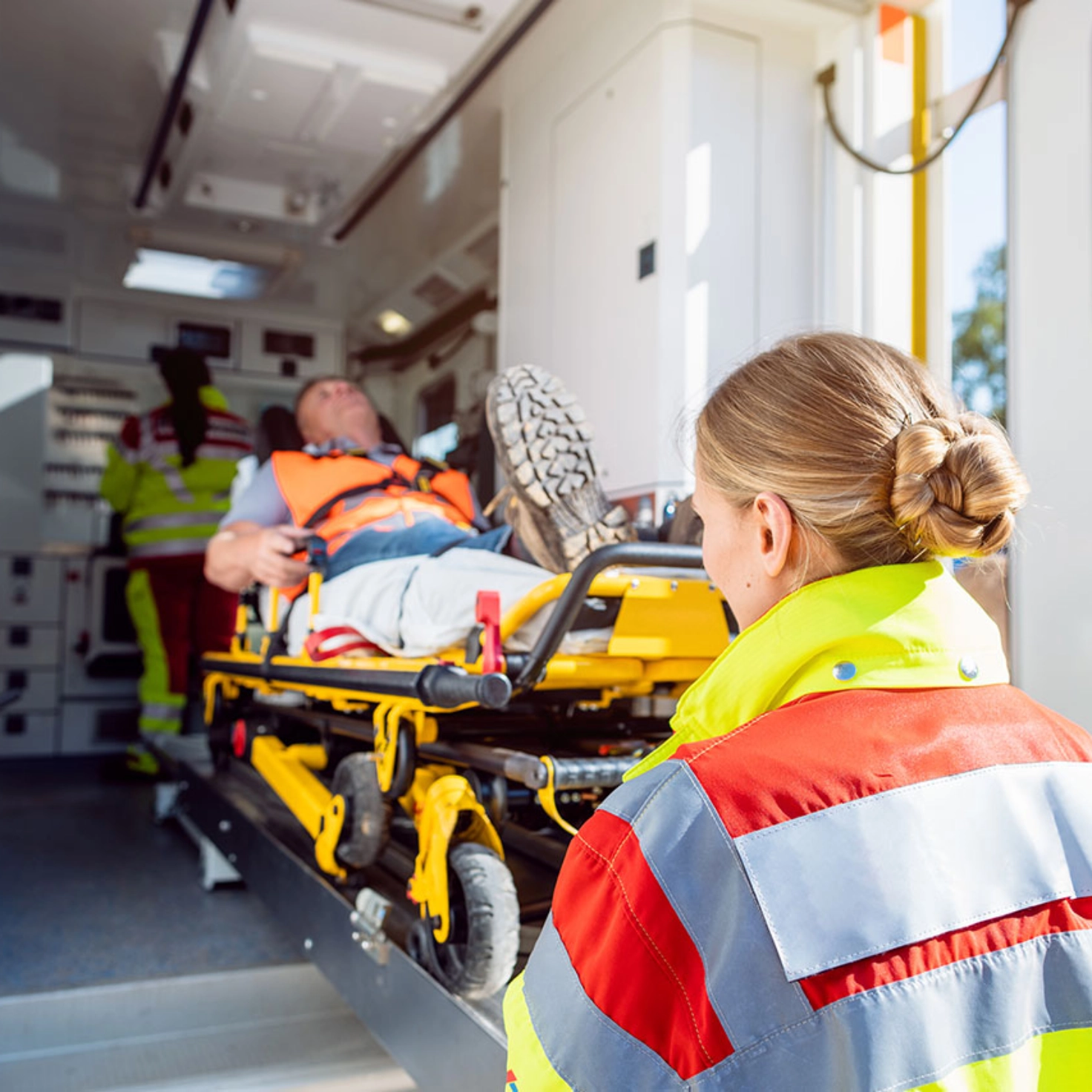 Eine Rettungssanitäterin schiebt den auf der Trage liegenden Patienten in den Rettungswagen