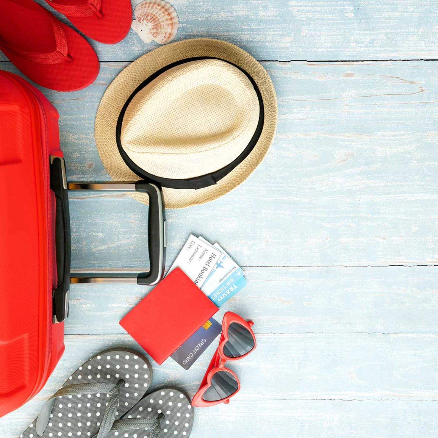 A suitcase lying on the floor with flip-flops, a hat and a passport next to it.
