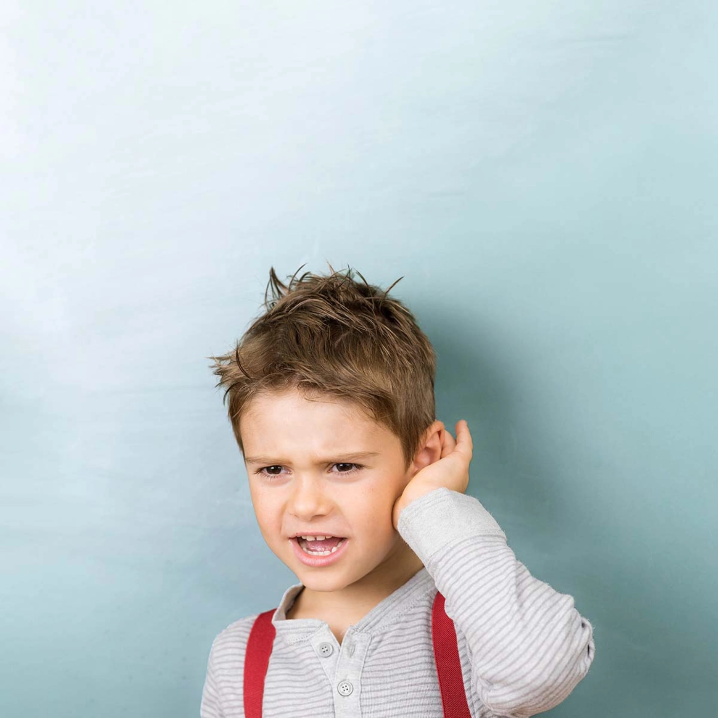 A boy with braces holds his hand to his ear.