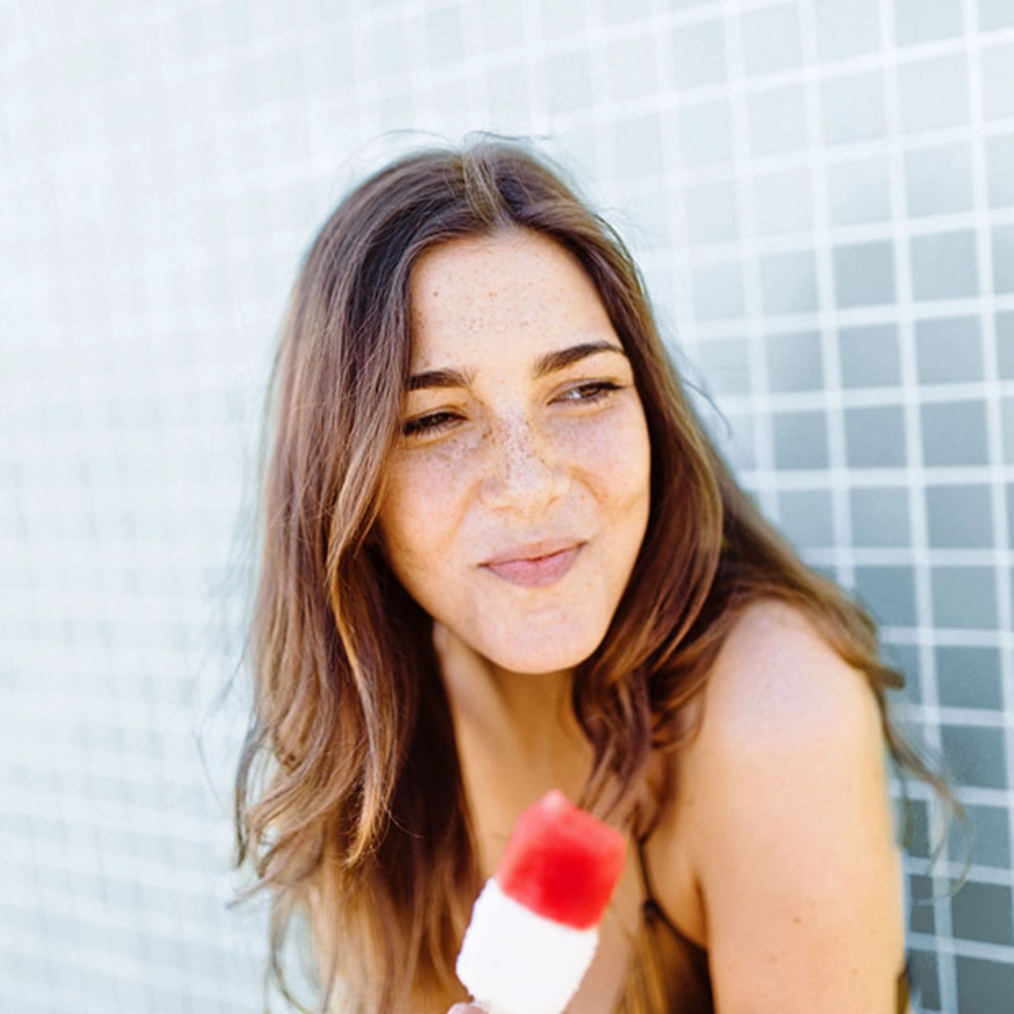 Eine junge Frau hält ein Eis am Stiel in der Hand und lächelt.