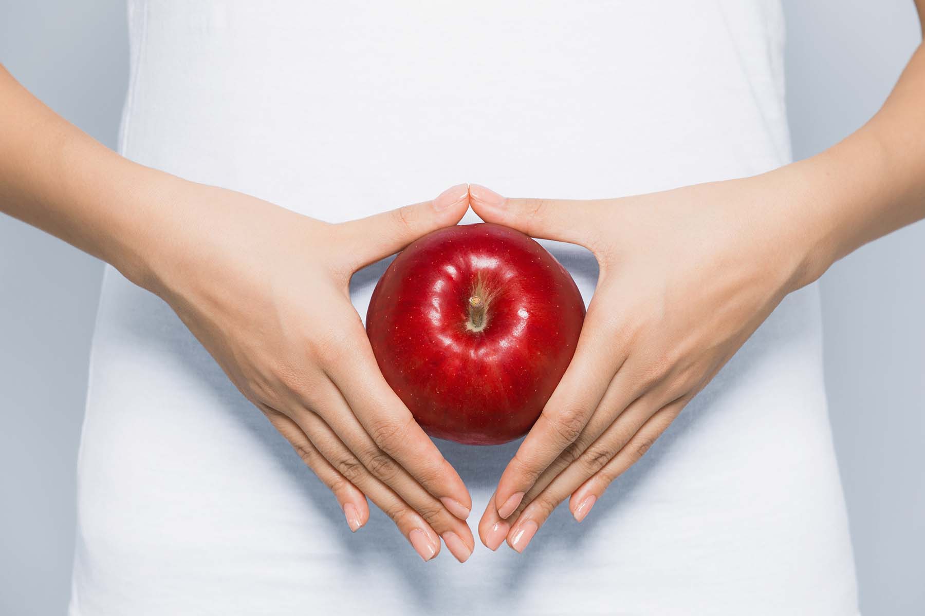 A woman holds an apple in front of her belly