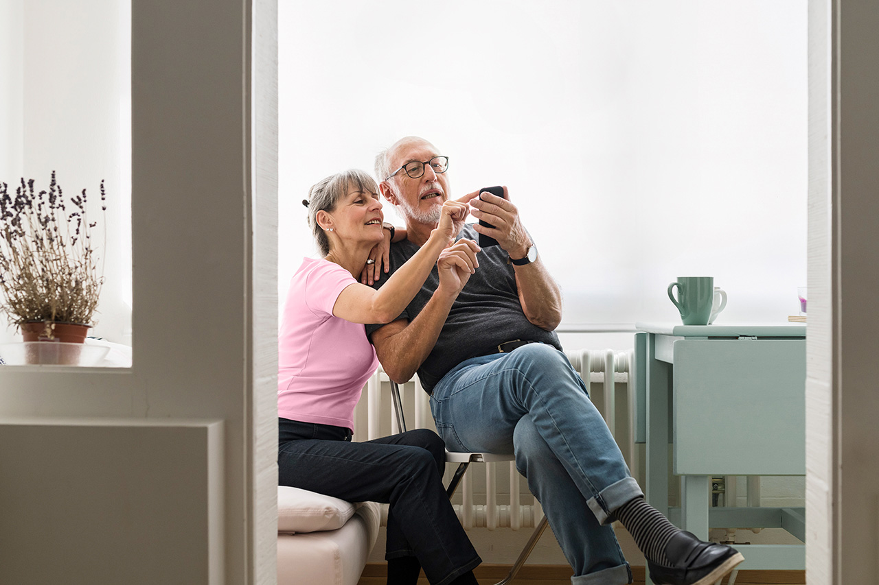 Un couple âgé est assis dans le salon et tape ensemble sur un téléphone portable.