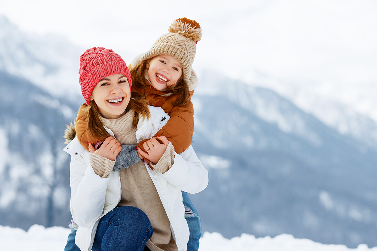 Mutter kniet im Schnee und Tochter umarmt sie von hinten