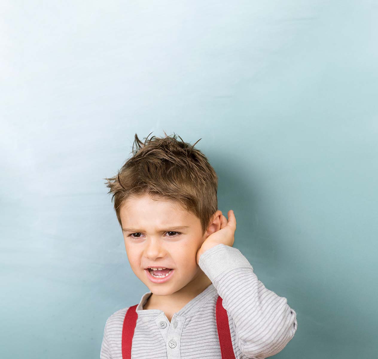 A boy with braces holds his hand to his ear.