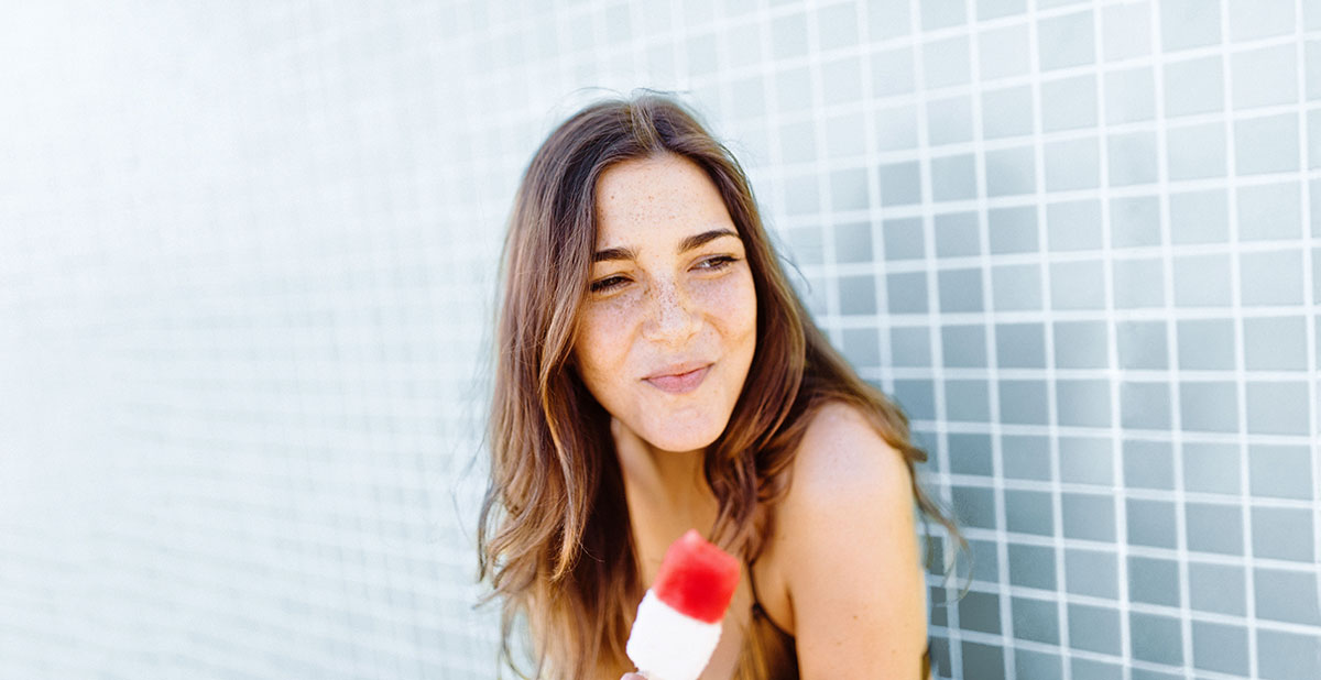 A young woman holds a popsicle in her hand and smiles.